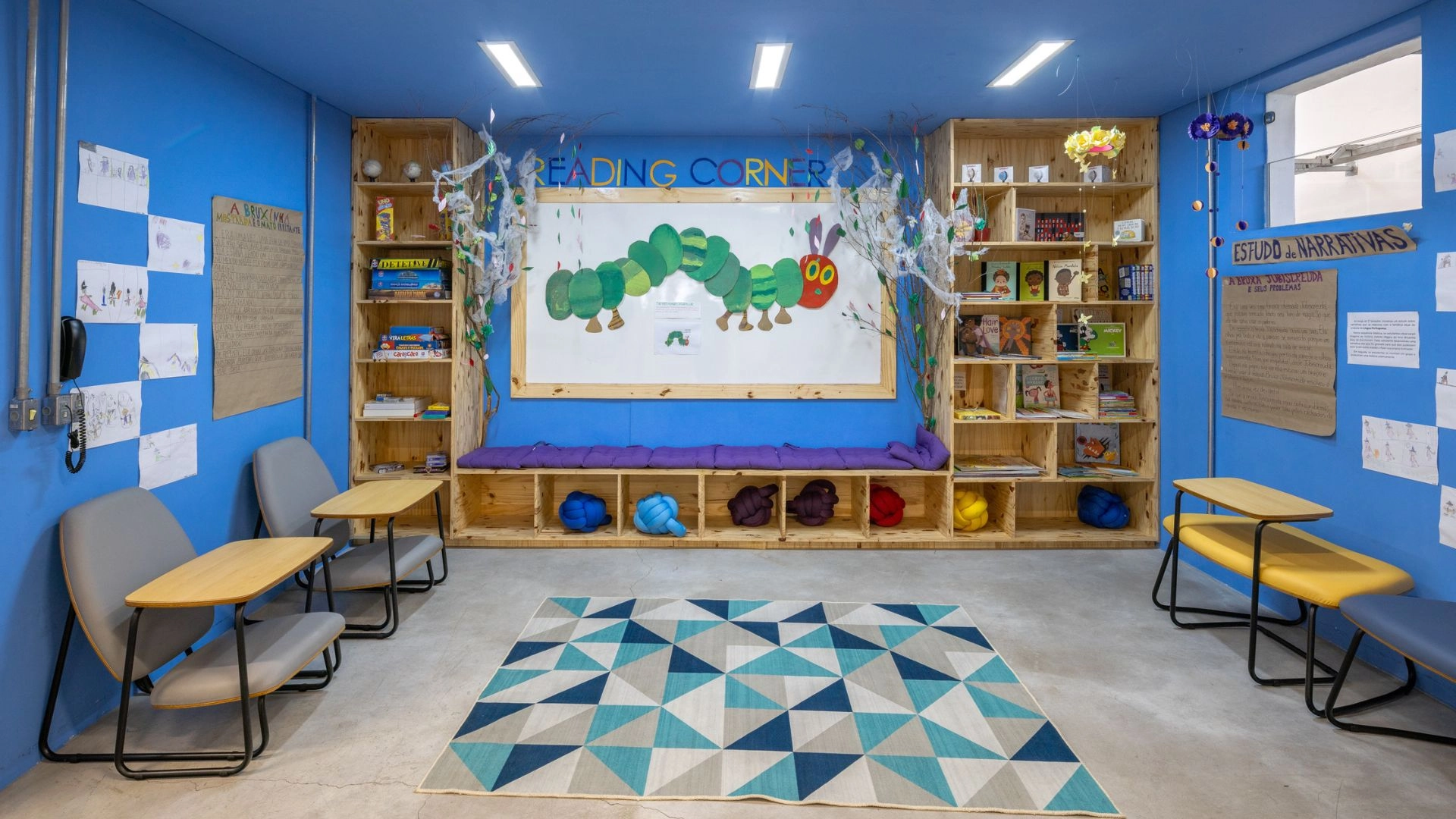Biblioteca da Trails School, o Reading Corner, com estantes de livros, banco com almofadas, tapete e painel da lagarta de The Very Hungry Caterpillar