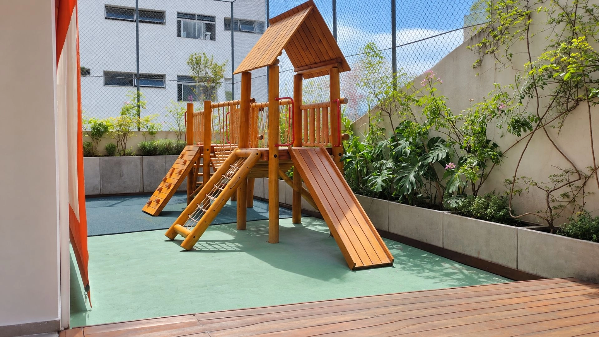 Parque da Trails School com brinquedo de madeira, escorregador e escada, cercado por plantas