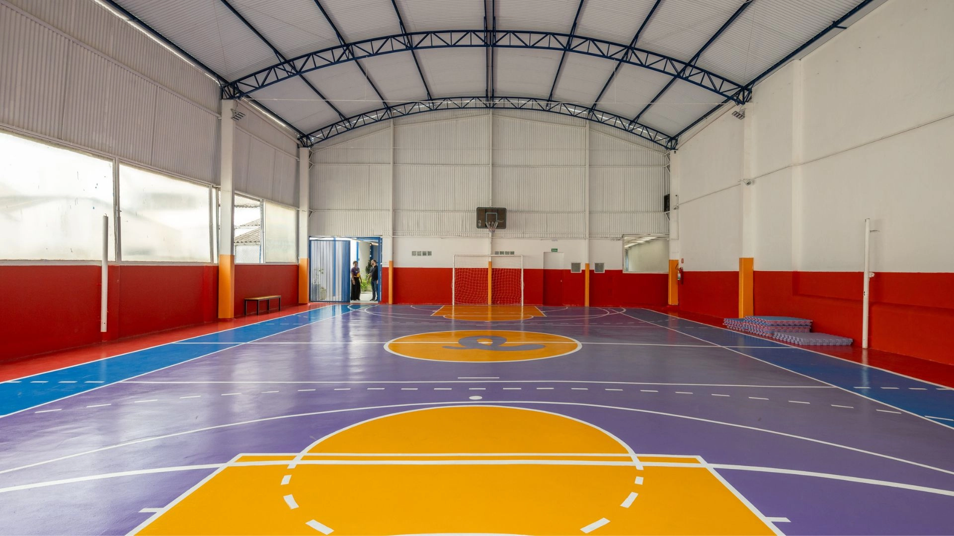 Quadra coberta da Trails School, com piso colorido, cesta de basquete e gol